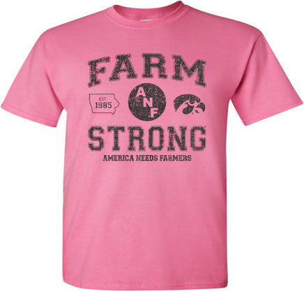 A pink short-sleeve t-shirt with a distressed black design on the front that reads 'FARM STRONG' with 'AMERICA NEEDS FARMERS' underneath, alongside the ANF logo and the Iowa Hawkeyes Tigerhawk logo.